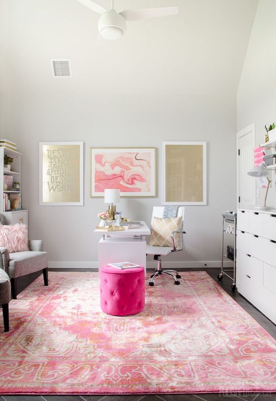 a bright home office with a hot pink ottoman, a pink rug and a gold and pink gallery wall