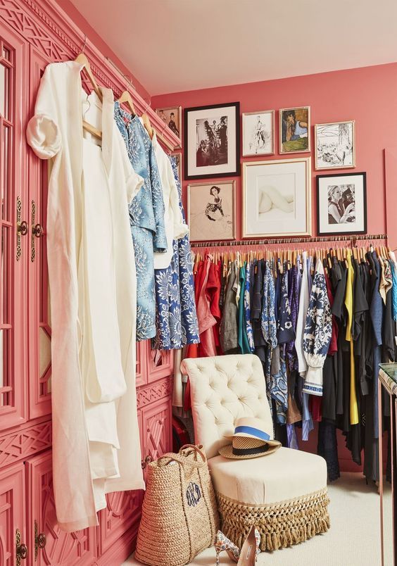 a bright pink feminine closet with wardrobes with mirror doors, a gallery wall, a makeshift closet and a beautiful neutral chair