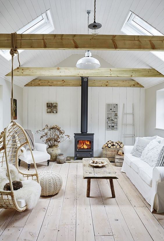a coastal barn living room in white, with wooden beams, a metal hearth, white seating furniture, reclaimed wood items and dried blooms