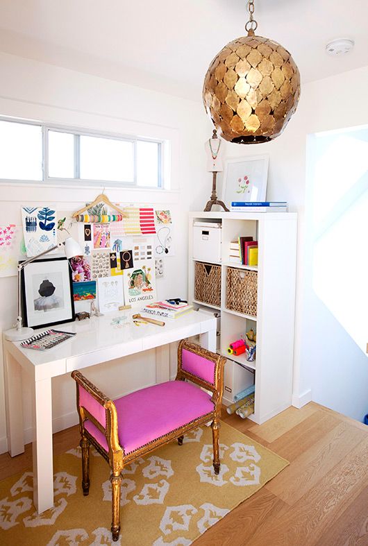 a colorful feminine home office with a hot pink stool, a gold scale pendant lamp and a bright gallery wall