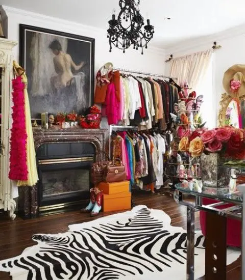 a colorful walk-in closet with open storage units, a fireplace, a zebra print rug, a black chandelier and a pretty glass vanity