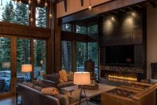a contemporary barn living room with glazed walls, a built-in fireplace, an incredible chandelier with multiple bulbs, leather seating furniture and table lamps