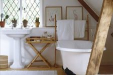 a cozy barn bathroom with white walls and a ceiling, stained wooden beams, a clawfoot tub and vintage furniture