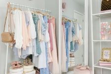 a cute pastel closet with light blue walls, an open makeshift closet, a large mirror, layered rugs, a pink stool and hats as decor