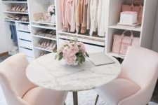 a delicate and subtle feminine closet with open shelves and storage units, pink chairs and a round stone table plus a crystal chandelier