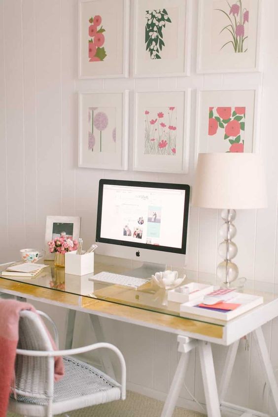 a feminine home office with a gold trestle desk, a white wicker chair and a colorful gallery wall plus touches of pink