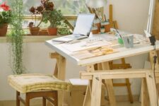a home artist studio with potted plants and succulents, a large stained desk, a stool, an easel and some artwork