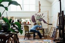 a light-filled artist studio with skylights and windows, easels, bookcases, storage shelves, potted plants, colorful artwork