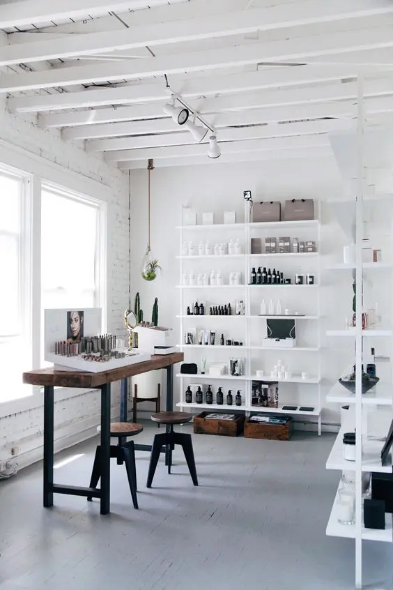 A light filled home artist studio with white open shelves, a tall desk and stools, some art and a lot of supplies