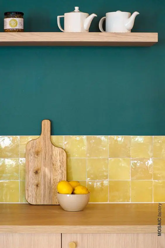 A light stained kitchen with dark green walls and a bold and shiny yellow tile backsplash plus an open shelf is a lovely idea