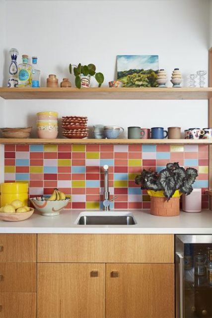 A light stained modern kitchen with white stone countertops and a colorful tile backsplash in pink, red, blue and yellow that creates a mood in the space