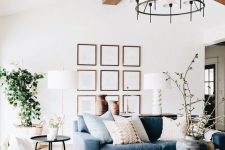 a lovely contemporary living room with wooden beams, a blue sofa, white chairs, a round coffee table, a chic chandelier and a potted plant