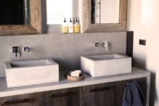 a minimalist barn bathroom with concrete walls, a weathered wood vanity, concrete sinks and mirrors in wooden frames