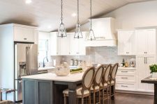 a modern barn kitchen with white shaker style cabinets, a grey kitchen island with a dining space, glass pendant lamps and lights