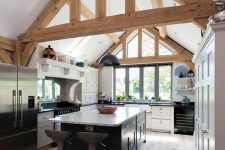a modern barn kitchen with wooden beams, white cabinets and a black kitchen island plus black appliances looks cool and fresh