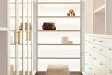 a neutral and very chic closet with drawers with glass doors, open shelves and drawers, open shelves and faux fur stools plus a crystal chandelier