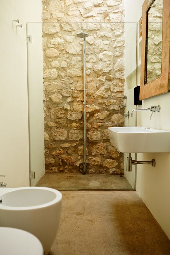 a neutral barn bathroom with a stone wall in the shower, a stone floor and modern appliances looks contrasting