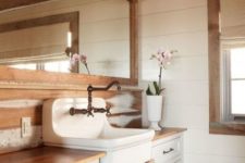 a neutral barn bathroom with wooden plank walls, a staiend ceiling, a white vanity and a vintage sink plus a large mirror