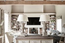 a neutral barn living room with a metal hearth, built-in shelves, neutral and pastel seating furniture, a whitewashed console table, wooden beams