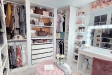 a pretty glam feminine closet with open storage units and drawers, a pink pouf and rug, a white vanity and a pink chair