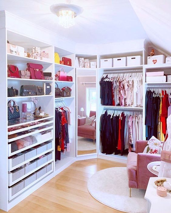 a prety and glam feminine walk-in closet with open storage units, boxes for storage, a full size mirror, a pink chair and a rug