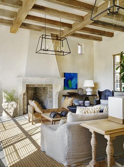 a refined barn living room with wooden beams, a fireplace clad with brick, neutral seating furniture, metal chandeliers and blue touches