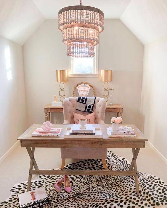 a refined feminine home office with wooden furniture, pink pillows, a printed rug and a statement chandelier