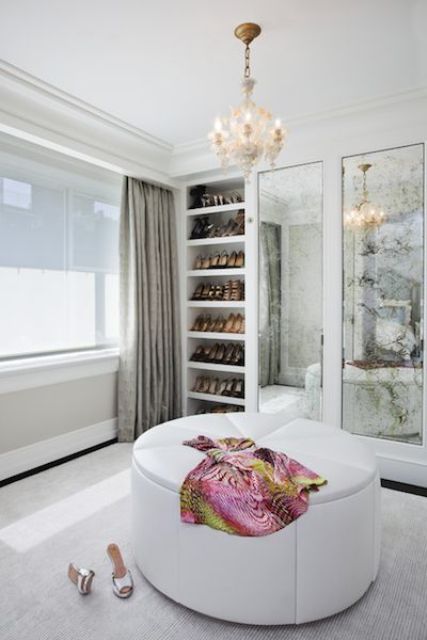 a refined modern closet in neutrals, with open show shelves, vintage mirrors, a white round pouf and a lovely chandelier