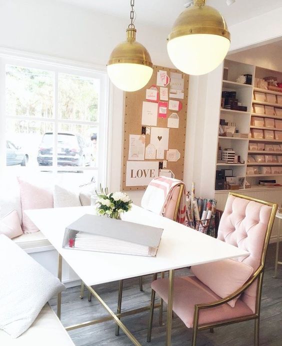 a romantic home office with an L-shaped bench, blush chairs, gold pendant lamps and a mood board