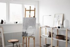 a serene Scandinavian home artist space with a large open storage unit, an easel, a stool, some artwork and some decor