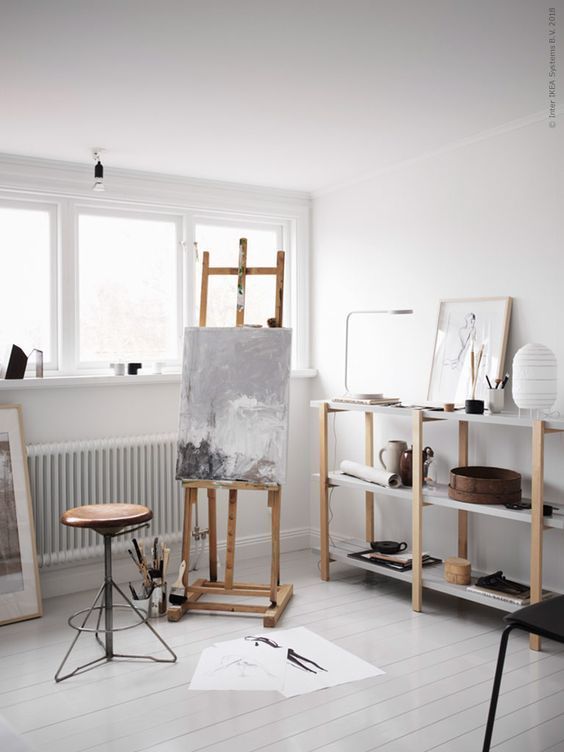 a serene Scandinavian home artist space with a large open storage unit, an easel, a stool, some artwork and some decor