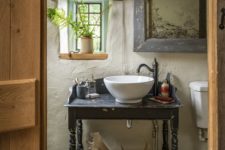 a shabby chic barn bathroom with white plaster walls, vintage furniture, a shabby floor and some greenery to refresh the space