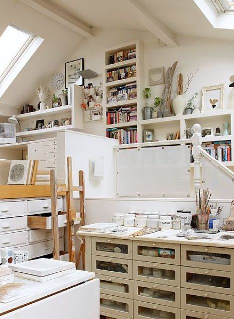 a small and cool art studio with skylights, lots of shelves and bookshelves, storage units, an easel and some decor