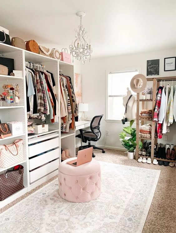 a stylish cloffice with open storage units, drawers and an open storage rack, a pink pouf, a white desk and a crystal chandelier