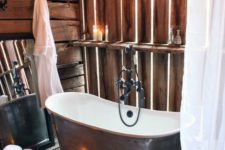 a vintage barn bathroom with wood all over it, a vintage metal tub, a sphere chandelier, candles and a wire basket