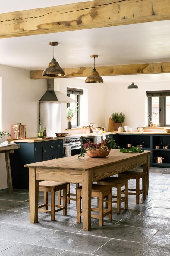 a welcoming barn kitchen with black shaker style cabinets and butcherblock countertops, a stained dining set and wooden beams