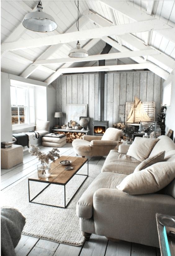 a whitewashed coastal barn living room with wooden beams, neutral seating furniture, a metal hearth, pillows and cushions