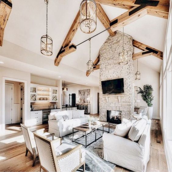 an airy barn living room with a brick fireplace, wooden beams, white seating furniture, a coffee table and lots of natural light incoming