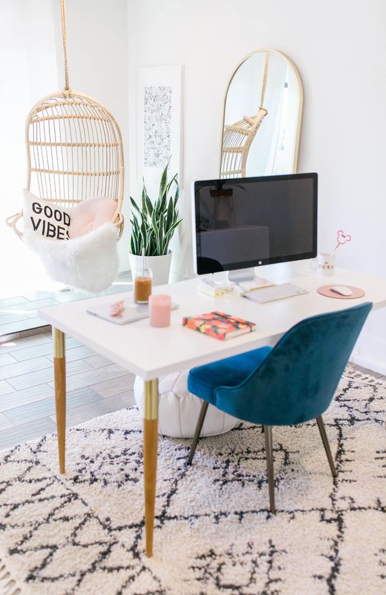 an airy feminine home office with a hanging rattan chair, a white desk, a navy chair and a statement mirror
