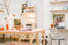 an airy home artist and craft studio with open shelves and decor, chairs and stools, a large table, some artwork and some plants