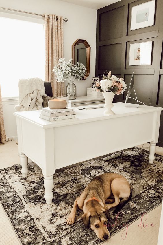 an elegant feminine home office with a black paneled wall, a white vintage desk, printed curtains and a rug and some blooms