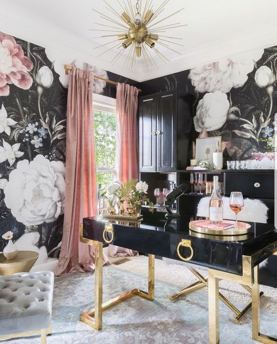 an exquisite feminine home office with floral walls, a black and gold desk, pink curtains and a gold burst chandeliers
