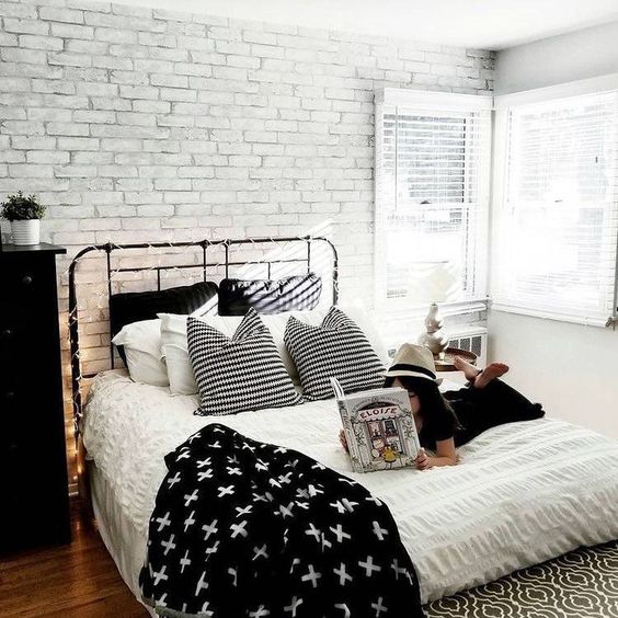 a Scandinavian bedroom with a faux white brick wall, a black metal bed and dresser, lights and monochromatic bedding