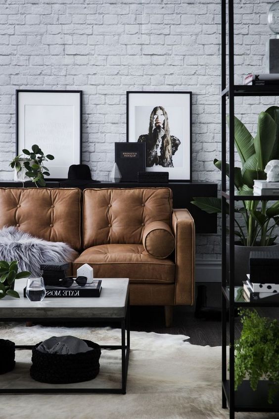 a Scandinavian living room in black and white, with a brown leather sofa and a white brick wall