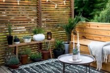 a backyard deck with built-in benches, potted greenery, lights and a screen for privacy is a great space to spend time