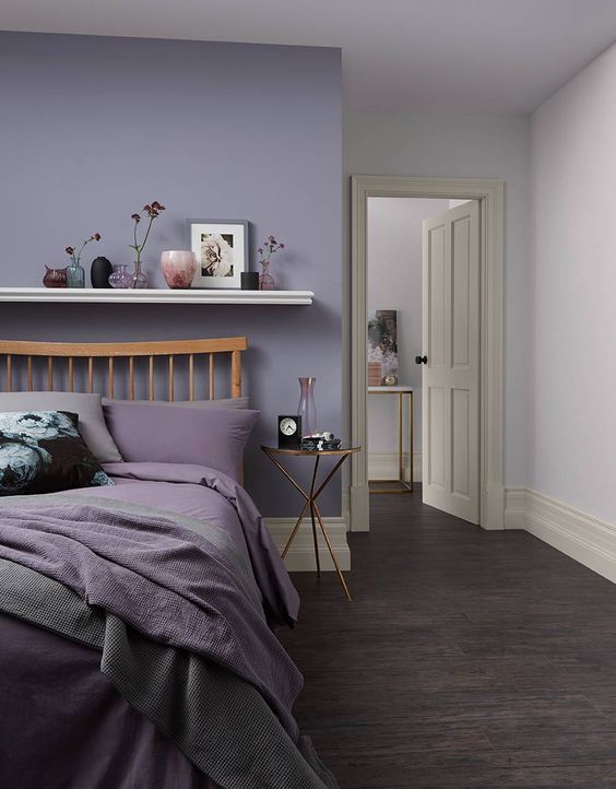a bedroom with a purple wall, a wooden bed with purple and grey bedding, lavender and white walls