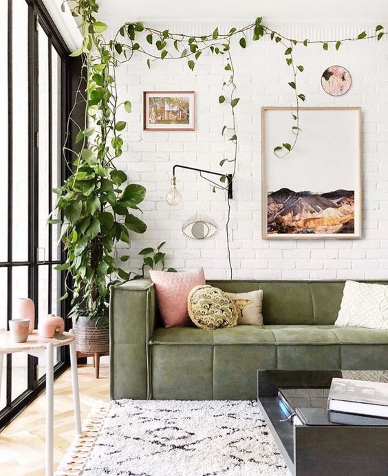 a boho chic living room with white brick walls, potted greenery, a green sofa and pink touches