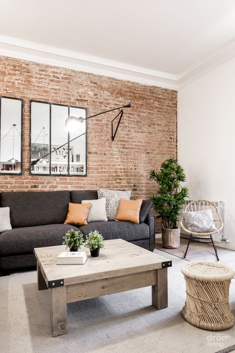 a boho living room with a red brick wall, rattan and wood furniture and an upholstered sofa