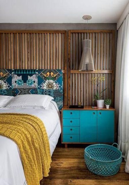 a bold and catchy bedroom with rich-stained panels on the walls, a bed with a printed headboard, a turquoise dresser, a wooden pendant lamp