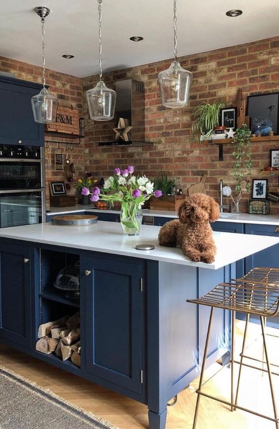 a bright blue kitchen with white countertops and glass pendant lamps is made bolder with red brick walls
